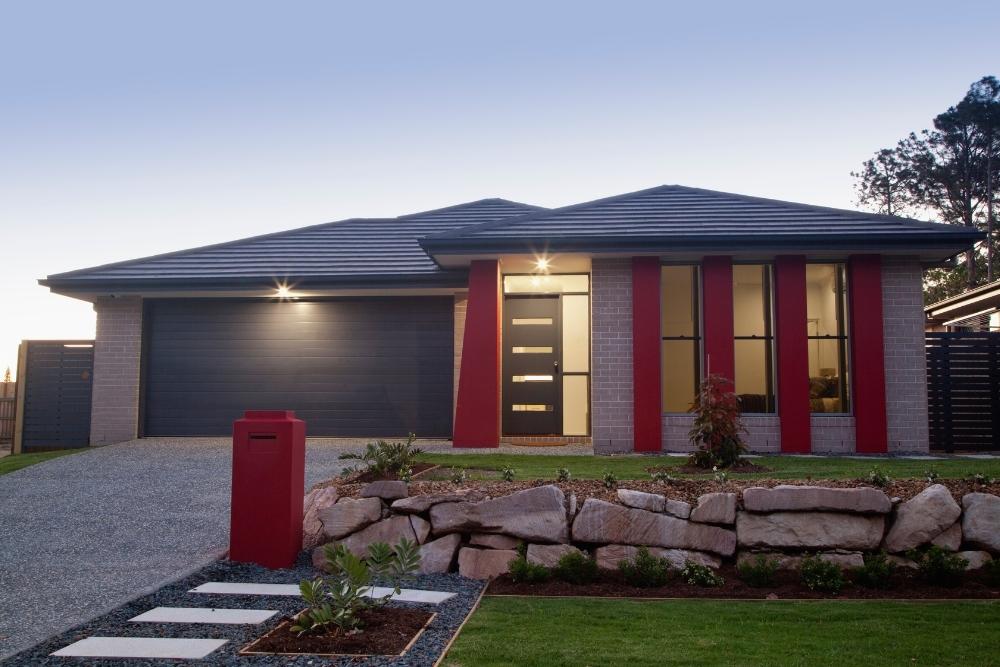 Modern single-storey residential home exterior featuring red accent pillars and a landscaped front garden-